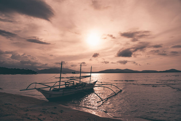 Puerto Princesa, Palawan, Philipines. Traditional Bangka catamaran boats in a bay in Palawan used by fishermen to go fishing. Almost sunset, magical ping orange light. - Fotó, kép