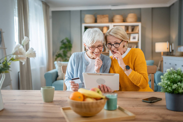 dvě starší ženy babička sestry nebo přátelé sedět doma používat kreditní debetní kartu pro on-line nakupování procházet internetové obchody na digitální tablet nákup věci sleva prodej skuteční lidé kopírovat prostor - Fotografie, Obrázek