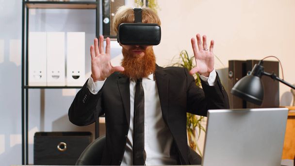 Fiatal szakállas üzletember programozó szoftver fejlesztő segítségével headset sisak app játszani szimulációs játék. Virtuális valóság megtekintése 3D 360 videó. Fiatal vörös hajú, VR szemüvegben, otthon dolgozik. - Fotó, kép