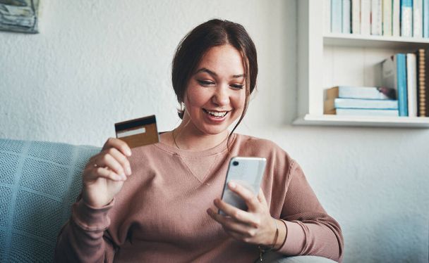 Ive never seen a discount I didnt like. a young woman using a smartphone and credit card at home - Foto, Bild