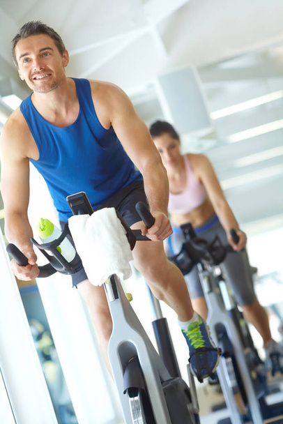 I can keep this up all day. A man and woman exercising in spinning class at the gym - Foto, Bild