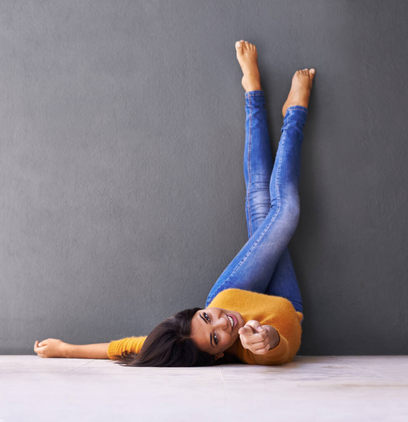 Keep calm and carry on. A young woman pointing at the camera while lying on the floor with her feet against the wall - Fotoğraf, Görsel