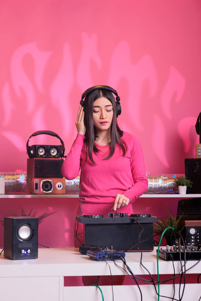 DJ masasında duran Asyalı müzisyen profesyonel karıştırıcı konsolu kullanarak remiks müzikle müzikal performans yaratıyor. Sanatçı tekno şarkı söylüyor, gece hayatının tadını çıkarıyor. - Fotoğraf, Görsel