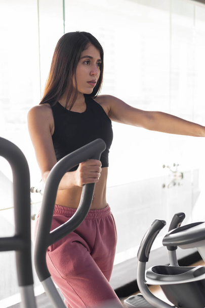 χρησιμοποιώντας μηχανήματα γυμναστικής μια νεαρή Λατίνα γυναίκα φορώντας αθλητικά ρούχα, ενεργό τρόπο ζωής για την ευεξία και την υγεία, την κατάρτιση δύναμης - Φωτογραφία, εικόνα