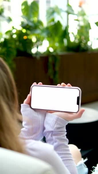 telefon s bílou obrazovkou reklamní prostor pro text detailní mladá dívka ruce vypadají radostně úsměv kavárna květináče příjemná atmosféra světlé oblečení teenager krásná mladá žena relaxace - Záběry, video