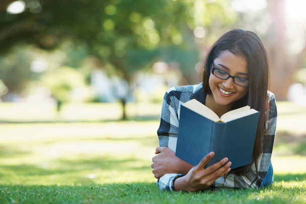 Relaxing with a good book. a young woman lying on grass and reading a book - Foto, Imagen