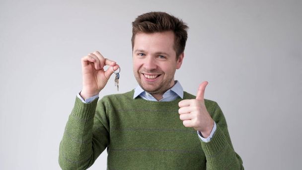 Młody Europejczyk pokazuje klucze do swojego nowego mieszkania. Cieszy się, że kupił własny dom. Zdjęcia studyjne - Zdjęcie, obraz