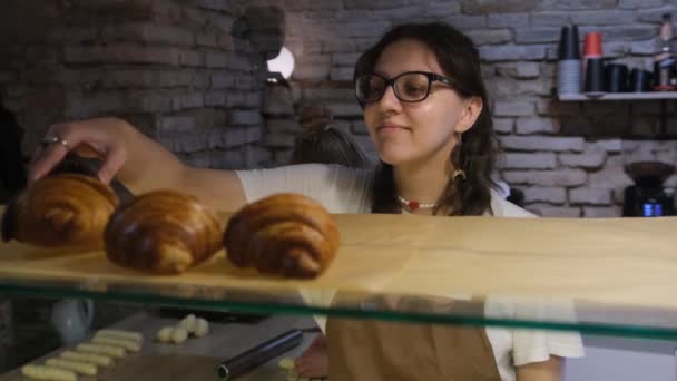 de meisjesverkoper zet croissants te koop op het bakkersraam. - Video