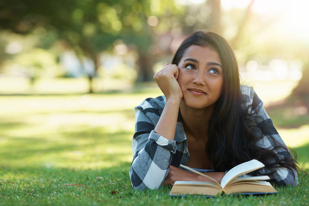 Se détendre avec un bon livre. une jeune femme allongée sur l'herbe et lisant un livre - Photo, image