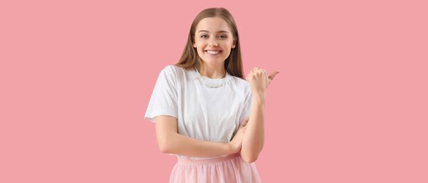 Happy young woman in t-shirt pointing at something on pink background - Photo, Image