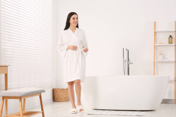 Beautiful happy woman wearing stylish bathrobe near tub in bathroom - Foto, Imagen
