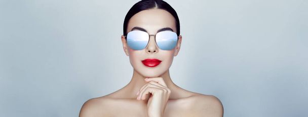 Attractive woman in stylish sunglasses on light grey background, banner design. Sky with clouds reflecting in lenses - Zdjęcie, obraz
