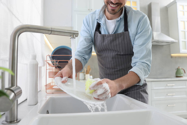 Man washing plate above sink in kitchen, closeup - Foto, imagen