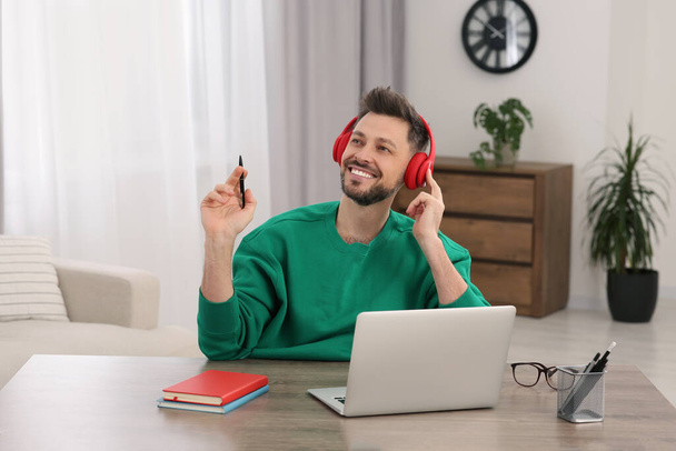 Man in headphones listening speaker at online translation course on laptop in room - Fotó, kép