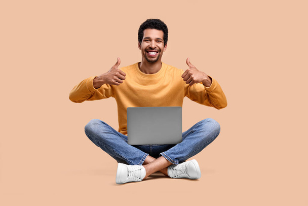 Happy man with laptop showing thumbs up on beige background - Foto, Imagem