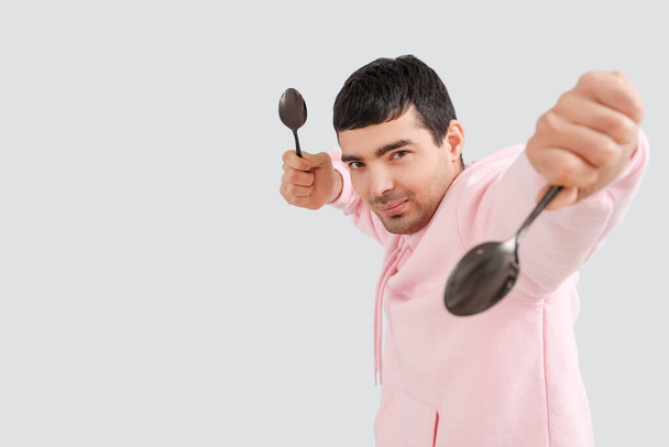 Junger Mann mit Esslöffeln auf grauem Hintergrund - Foto, Bild
