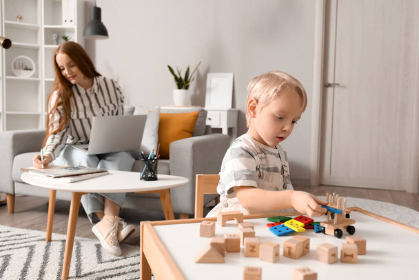 Cute little boy playing with wooden toys while his mother working at home - Foto, imagen