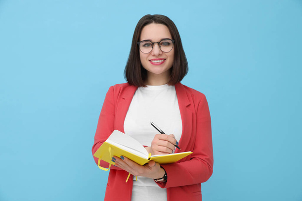 Happy young intern with notebooks and pen on light blue background - Foto, imagen