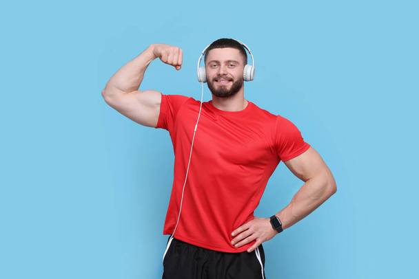 Handsome man with headphones showing muscles on light blue background - Фото, изображение