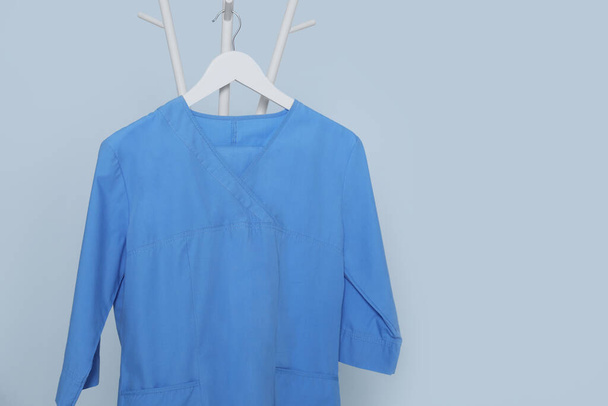 Blue medical uniform hanging on rack against light grey background. Space for text - Foto, imagen