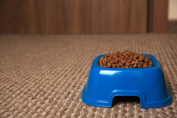 Dry pet food in feeding bowl on soft carpet indoors. Space for text - Foto, imagen