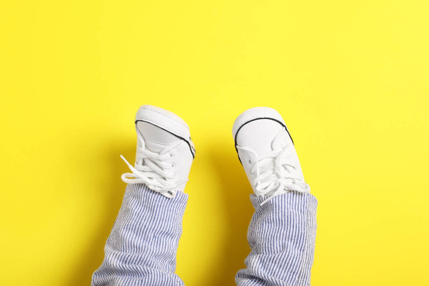 Little baby in stylish gumshoes on yellow background, top view. Space for text - Φωτογραφία, εικόνα