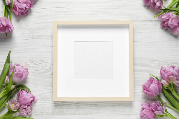Empty photo frame and beautiful flowers on white wooden table, flat lay. Space for design - Fotografie, Obrázek