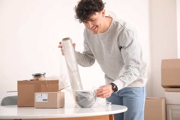 Junger Mann wickelt Schalen in Küche mit Stretchfolie ein - Foto, Bild