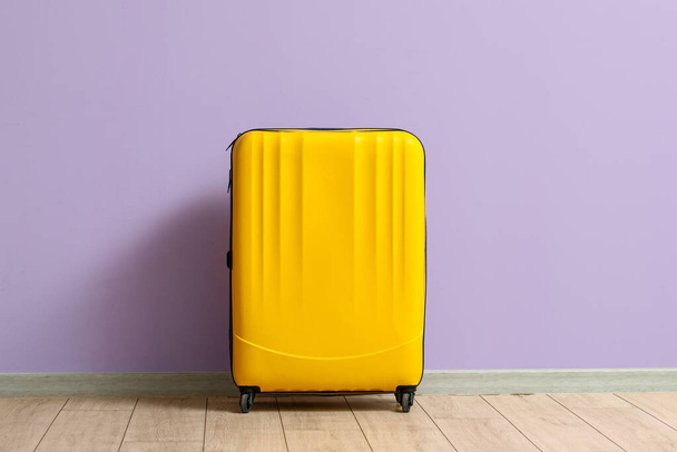 Yellow suitcase near lilac wall - Фото, изображение