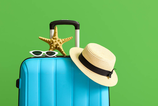 Maleta con sombrero, gafas de sol y estrellas de mar sobre fondo verde - Foto, imagen