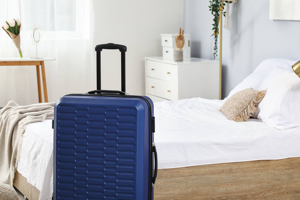 Blue suitcase near bed in light room - Фото, изображение