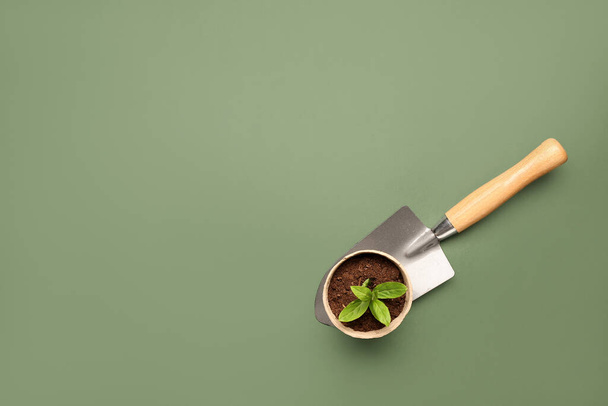 Торфяной горшок с зелеными саженцами и лопатой на зеленом фоне - Фото, изображение