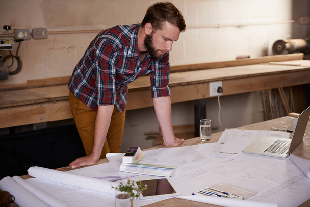 Design pro at work. молодой мужчина-архитектор, работающий над строительными планами в своей мастерской - Фото, изображение