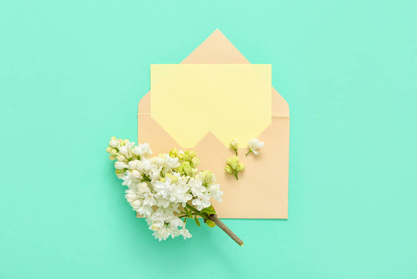 Envelope with blank card and lilac flowers on turquoise background - Photo, Image