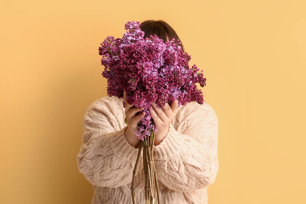 Young woman with bouquet of lilac flowers on yellow background - Foto, afbeelding
