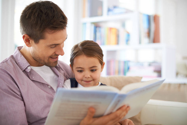 Η εκπαίδευση ξεκινά από το σπίτι. Ένας νεαρός πατέρας διαβάζει ένα βιβλίο με την κόρη του. - Φωτογραφία, εικόνα