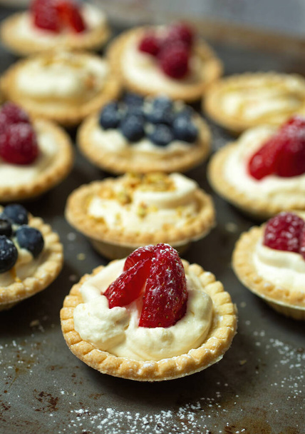 Strawberry tartlet with blueberry, raspberry and pistachios tartlets on a metal plate and powder sugar - Foto, imagen