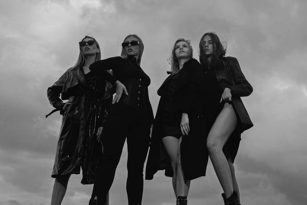 Fashion portrait of group fashion models girls posing outdoor, black style outfit against sky. Attractive young vogue women - Foto, Imagen
