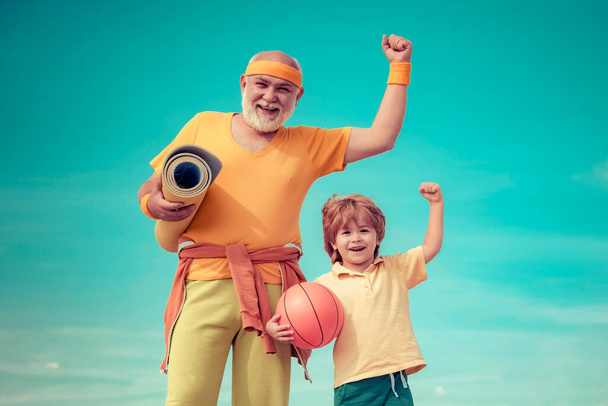 Elderly sporty man and young boy sporting morning workout - copy space. Young - old workout. Portrait of a healthy father and son working out over blue sky background - Foto, Imagem