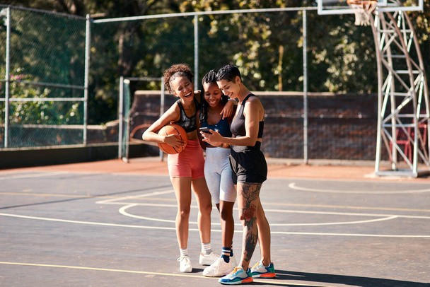 Eso se ve muy gracioso. un grupo diverso de deportistas de pie juntos después de jugar baloncesto y mirando un teléfono celular - Foto, imagen