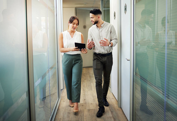 Let me update you. Full length shot of two young businesspeople walking through the office and having a discussion while using a digital tablet - Zdjęcie, obraz