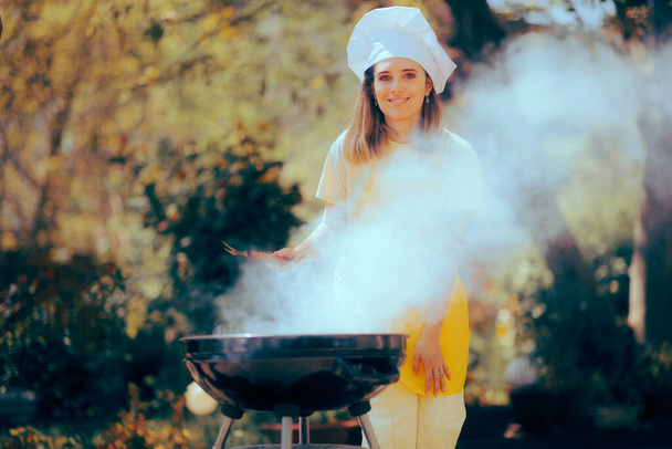 Happy Woman Wearing Yellow Apron Cooking on a Grill Outdoors - Foto, Imagen