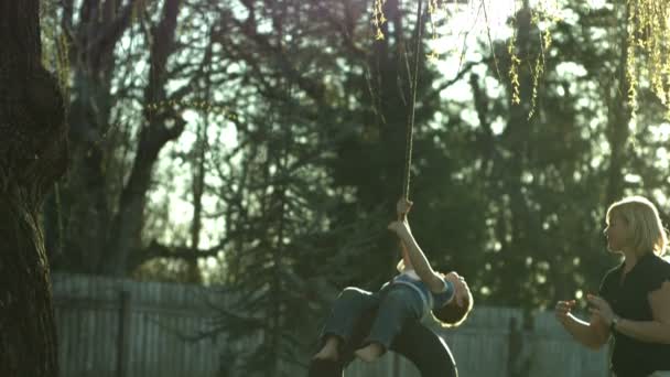 Mom pushing son on tire swing - Materiał filmowy, wideo