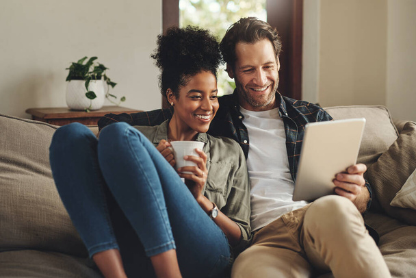 Relax, home and interracial couple on a couch, tablet and happiness with social media and connection. Partners, man and woman on a sofa, technology and loving with a smile, romance and online reading. - Foto, immagini
