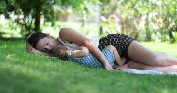 Mom resting with baby laid on grass outside - 写真・画像
