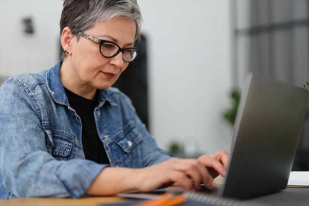 Senior woman in glasses works on a laptop. - Valokuva, kuva