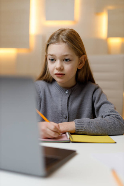 A little girl is studying remotely on a desktop behind a laptop. - Fotó, kép