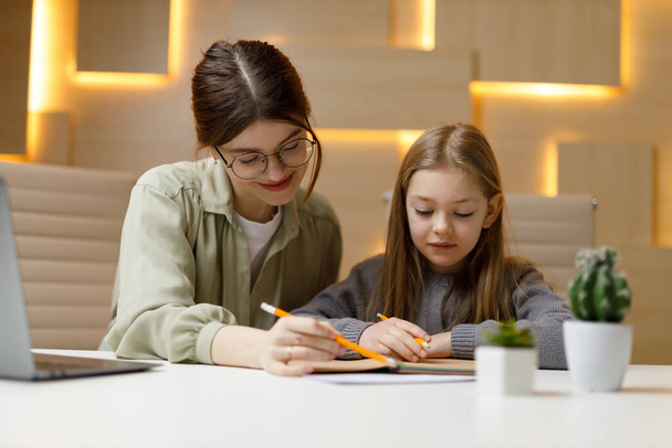 Teacher and student at the desk, mother helps her daughter do homework, private children's tutor. - Fotoğraf, Görsel