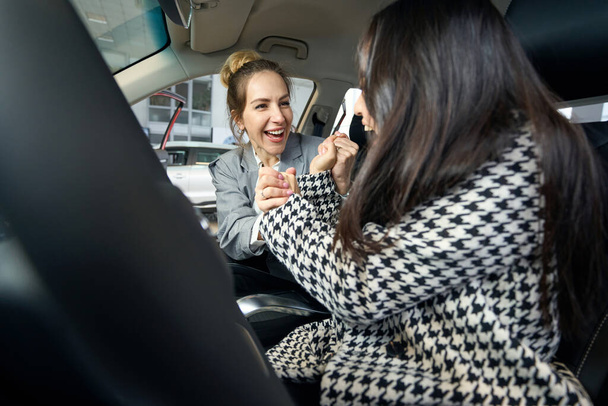 Δύο ευτυχισμένες γυναίκες με κοστούμια κρατιούνται χέρι-χέρι και κάθονται στο αυτοκίνητο. - Φωτογραφία, εικόνα