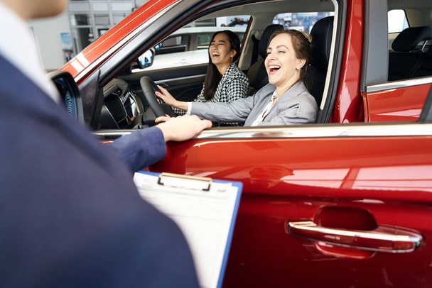 Zwei lachende Damen sitzen in rotem Auto auf den Vordersitzen - Foto, Bild